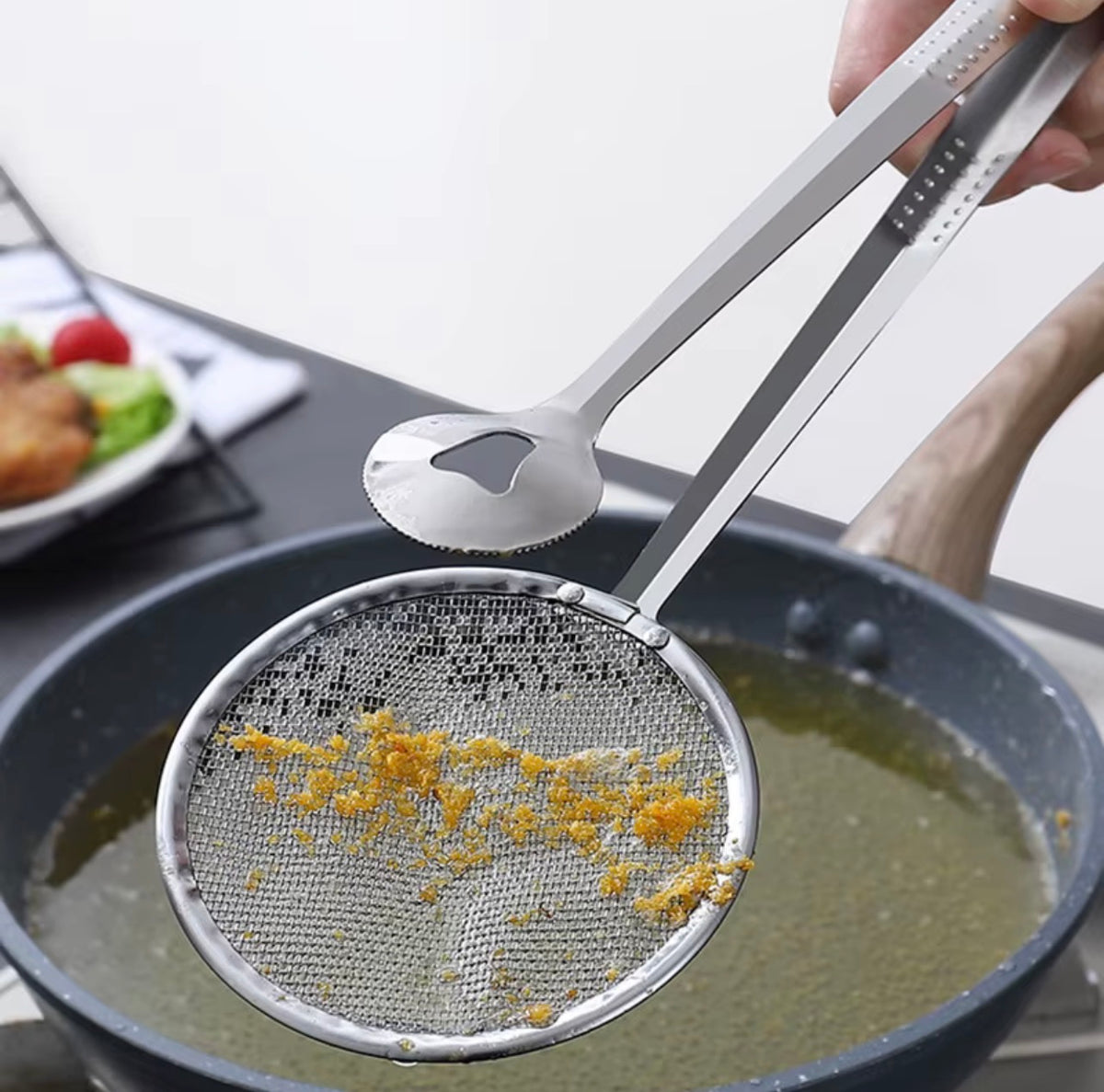 Fine mesh oil strainer tongs removing food particles from frying oil