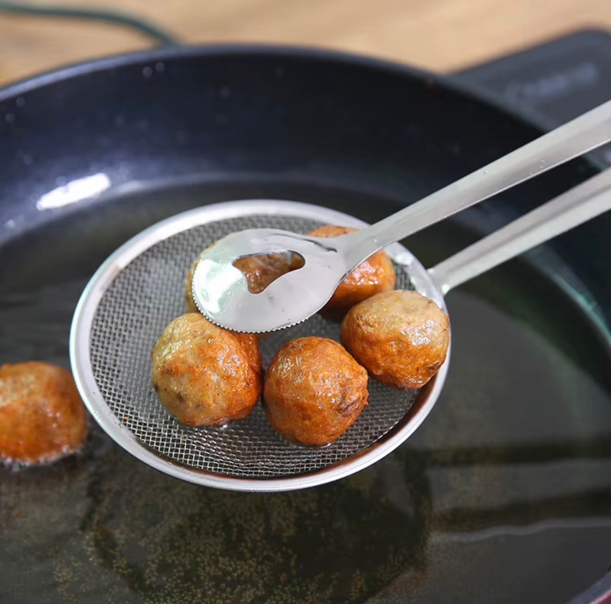 Stainless steel mesh strainer tongs holding fried food above cooking oil